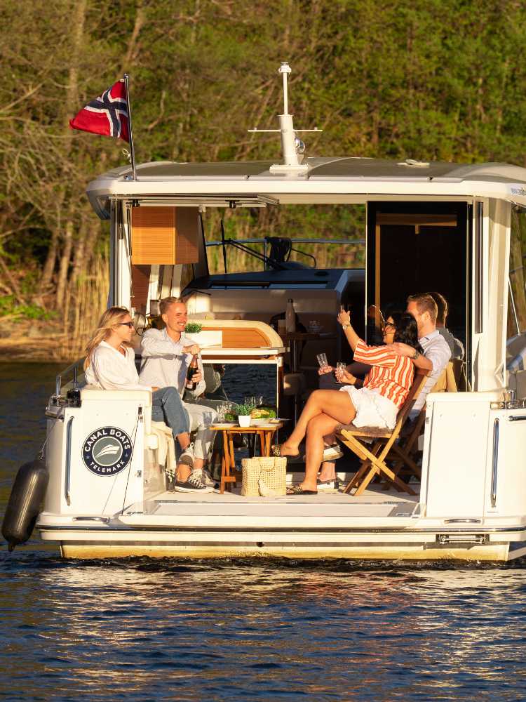 Four people enjoying drinks on a boat in an autumn setting on a lake.