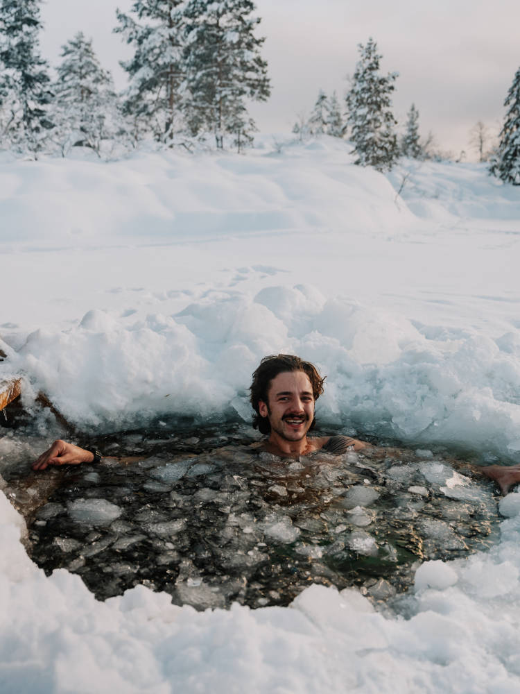 Man enjoying an ice bath in a hole before Vrådal Panorama Sauna, with a view of the winter panorama.