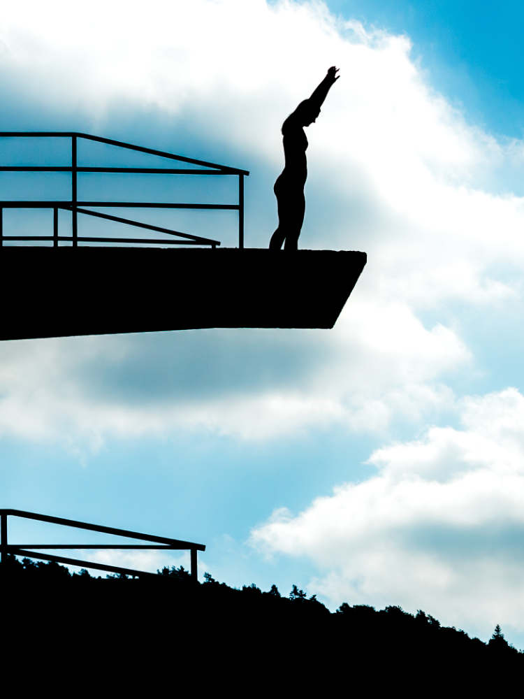 Silhouette of a woman on a 10m diving tower, beautifully backlit by the sun, capturing the graceful anticipation of a high dive.