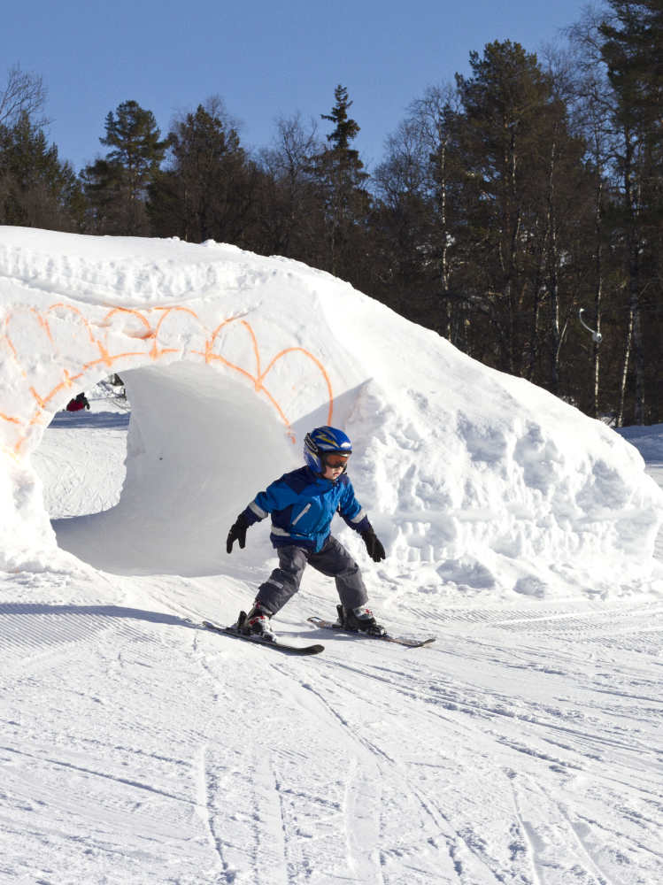 Child skiing through a hole in a snow mound
