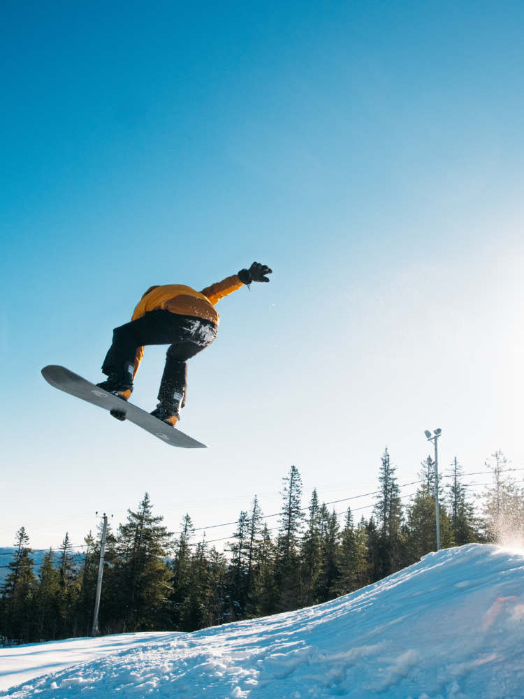 Snowboarder jumping over a ski ramp against a blue sky
