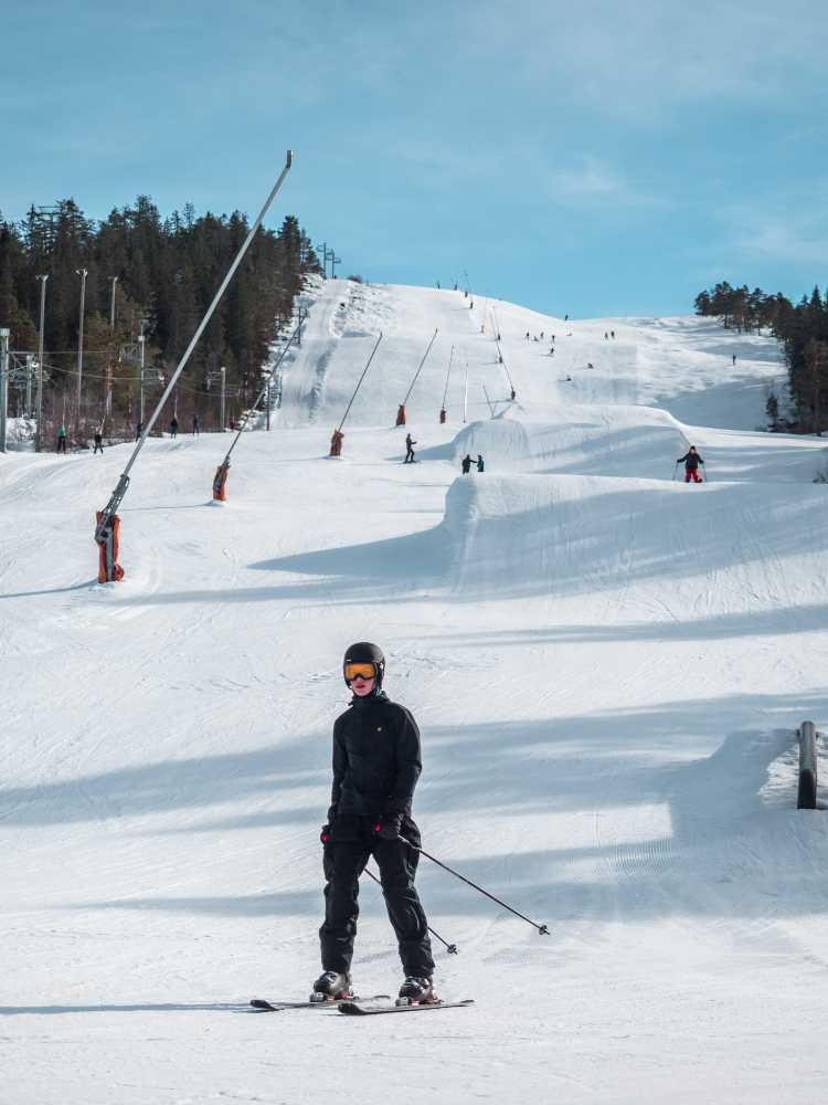Skier descending a slope with ski jumps in the background under a blue sky